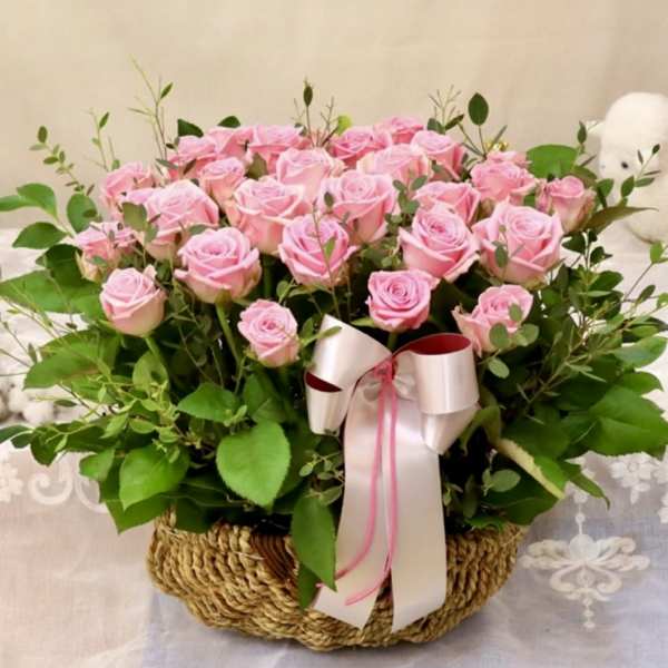 Pink roses arranged in a woven basket with a ribbon bow
