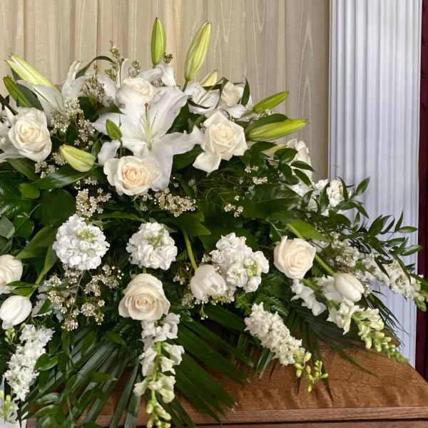 Large white floral spray with lilies and roses on a casket