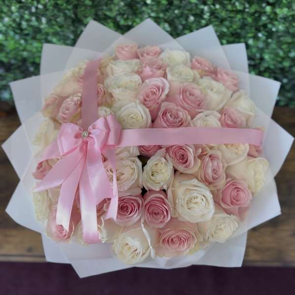Bouquet of pink and white roses wrapped in white paper with a pink ribbon