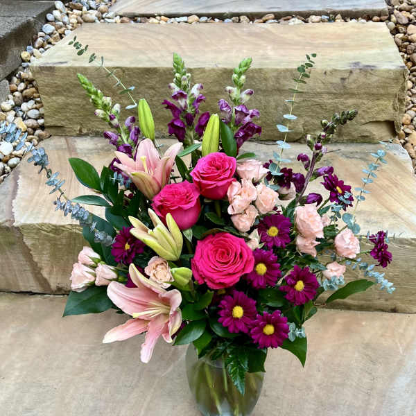 Bouquet of pink roses, lilies, and purple daisies in a glass vase