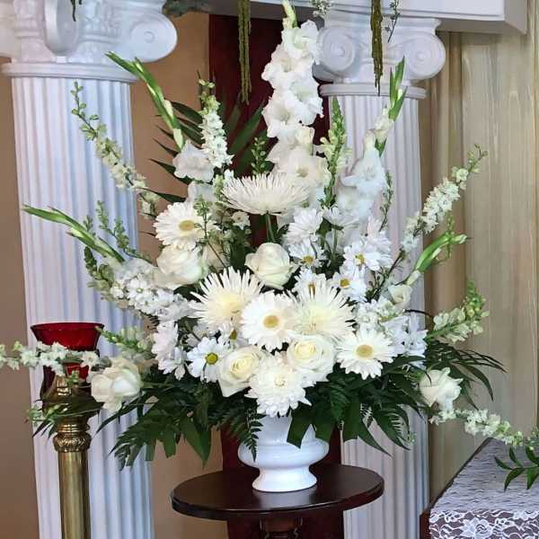 Large all-white arrangement of roses, daisies, and mums in a white pedestal vase