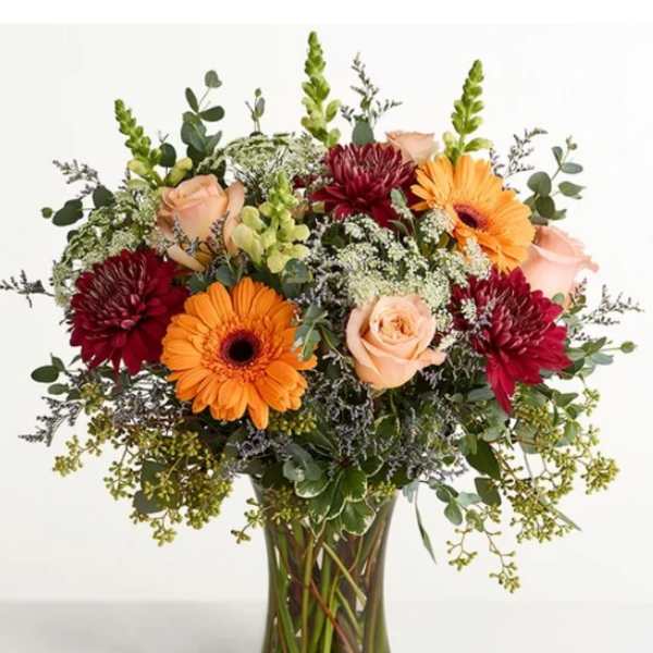 Mixed bouquet of orange gerbera daisies, peach roses, and burgundy mums in a glass vase