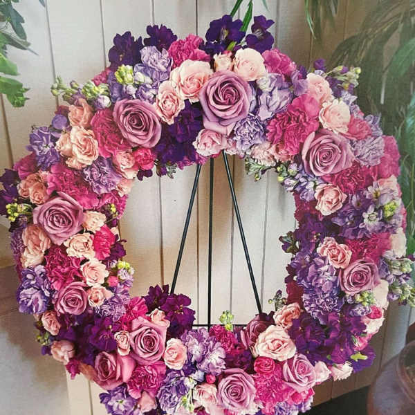 Heart-shaped floral wreath in pink, lavender, and purple blooms on a black stand