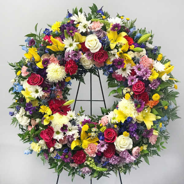 Large circular floral wreath with mixed colorful flowers on a stand