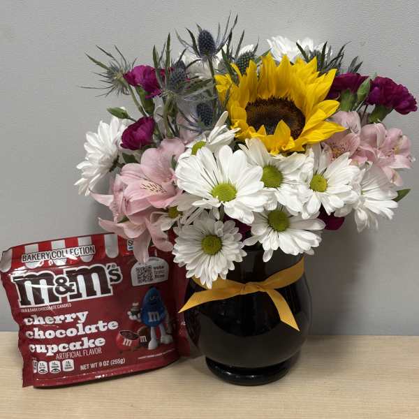 Mixed bouquet in a black vase with a bag of M&M's candy beside it