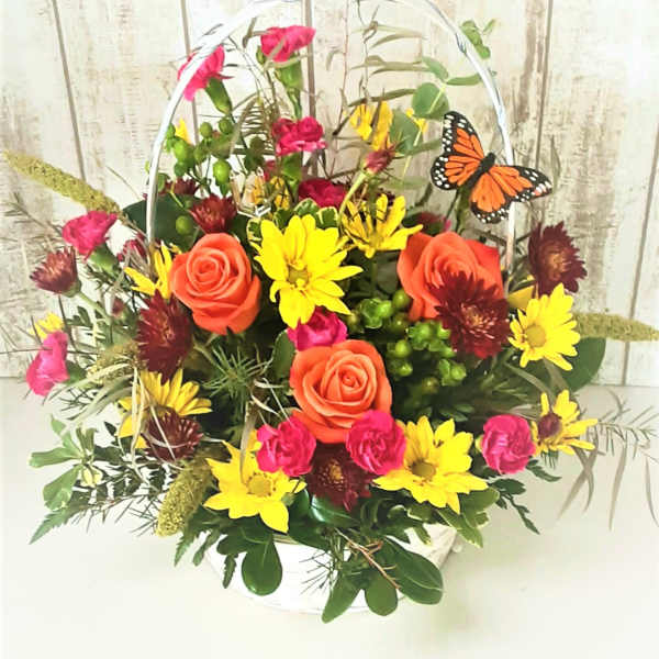 Basket arrangement of orange roses, yellow daisies, and pink flowers with a butterfly pick