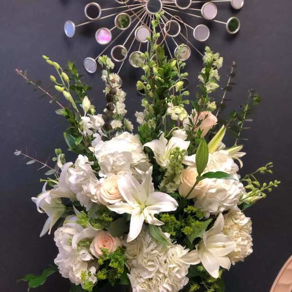 White floral arrangement in a glass vase with lilies, roses, and hydrangeas