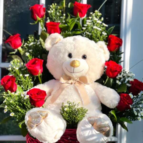 Red roses arranged around a teddy bear in a basket