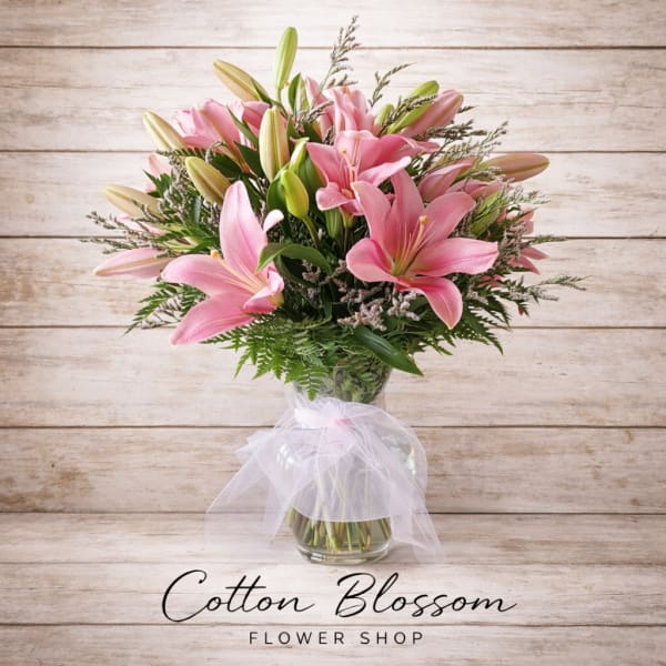Pink lilies arranged in a glass vase with a white ribbon