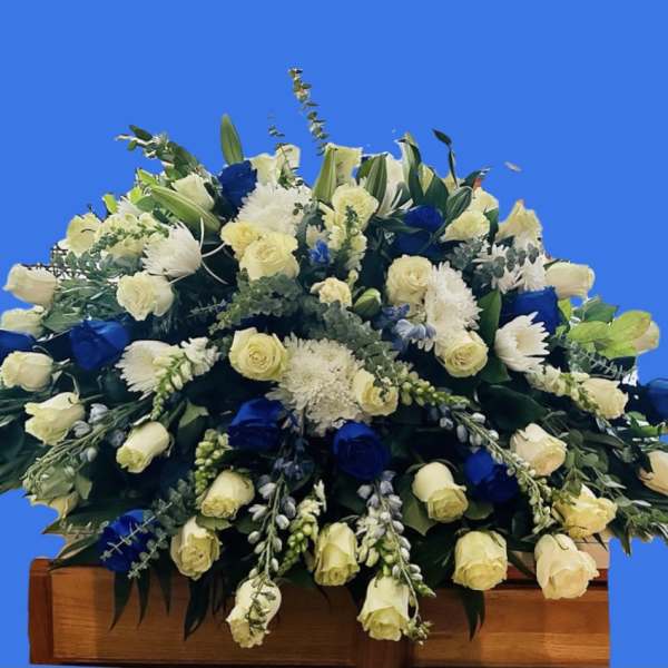 Large funeral spray of white and blue flowers on a wooden stand