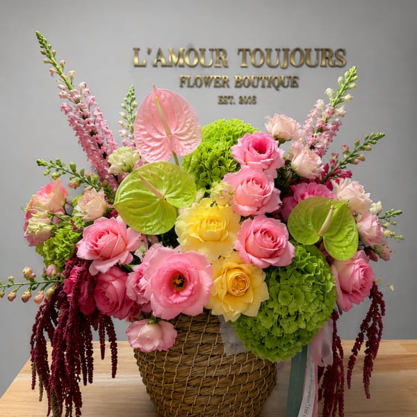 Pink and yellow floral arrangement in a wicker basket with green accents