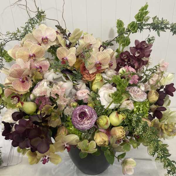 Large mixed orchid arrangement in a dark vase with pale and deep purple blooms