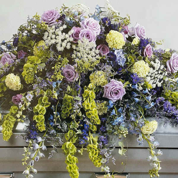 Lavender and blue floral casket spray with trailing greenery