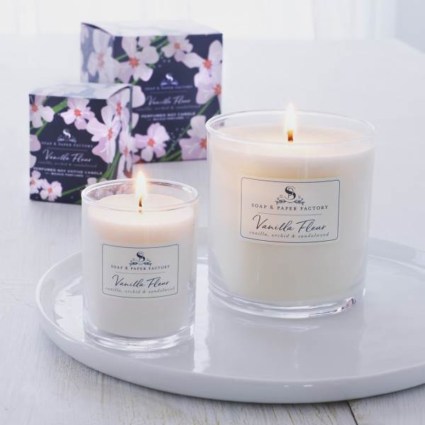 Two lit vanilla candles in glass jars with floral boxes behind them
