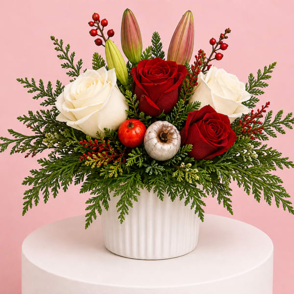 Red and white roses in a white vase with evergreen accents and berries
