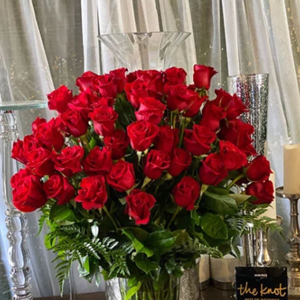 Tall vase arrangement of red roses with greenery