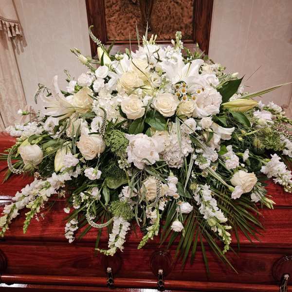 Large white floral spray on a polished wooden casket