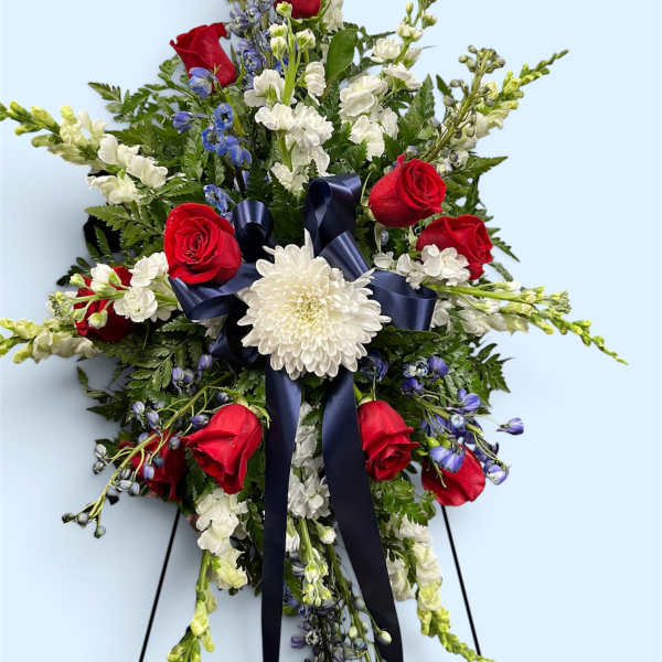 Standing floral spray with red roses, white blooms, and a navy ribbon