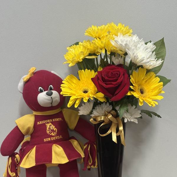 Bouquet of yellow and white daisies with a red rose in a black vase beside a teddy bear