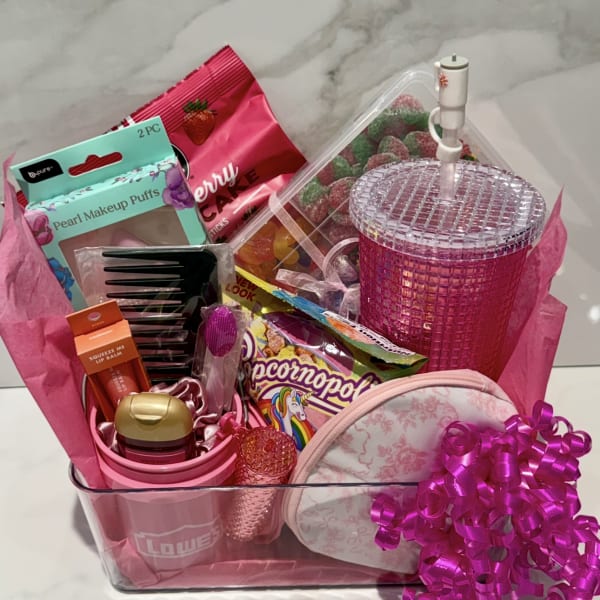 Pink gift basket with candy, makeup items, and a glittery tumbler