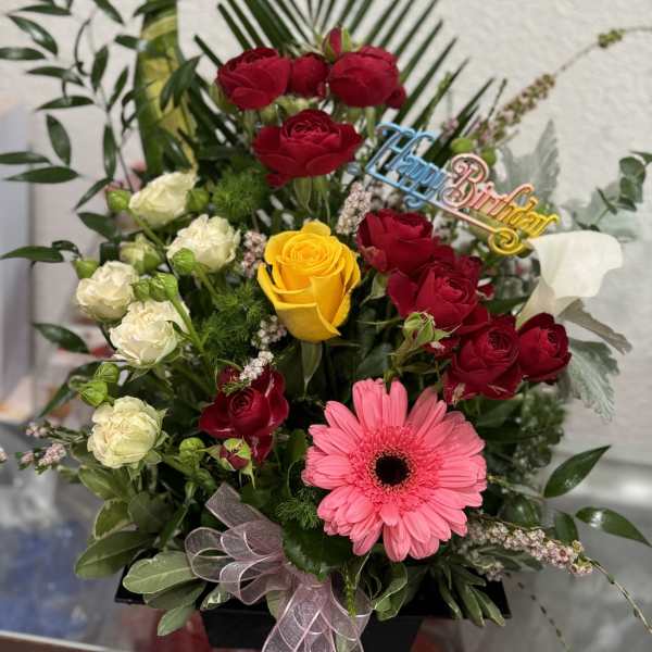 Mixed bouquet of red and yellow roses with a pink gerbera daisy in a black box