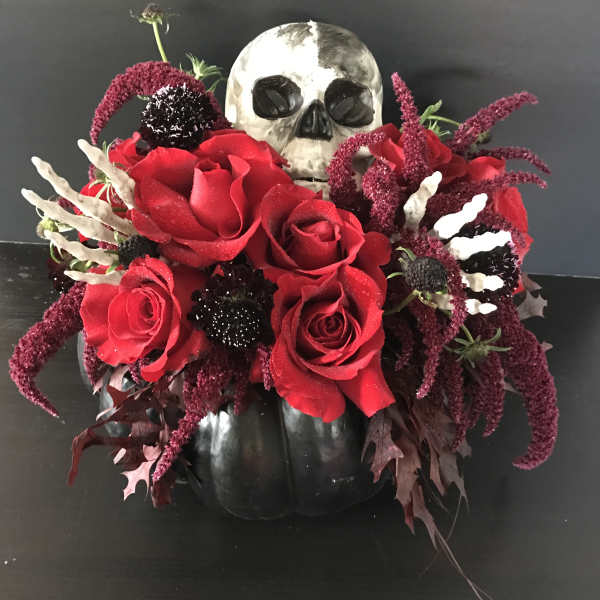 Red roses arranged around a skull in a black pumpkin container