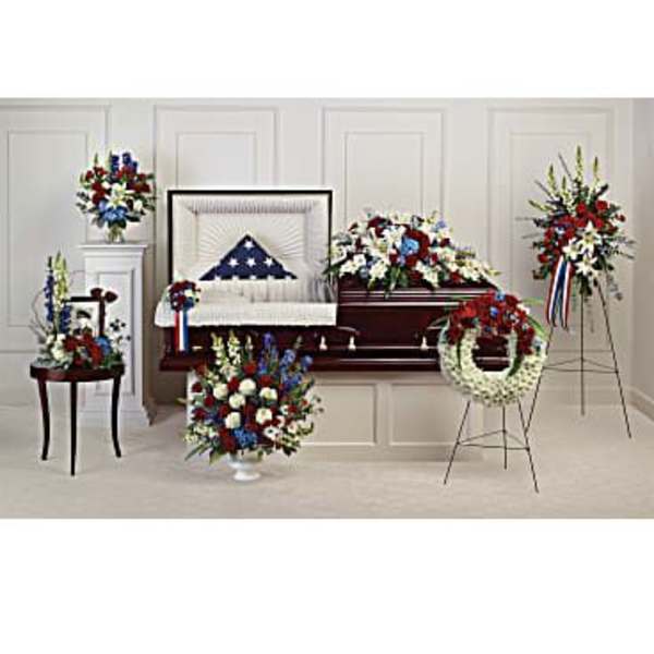 Funeral casket surrounded by red, white, and blue floral sprays