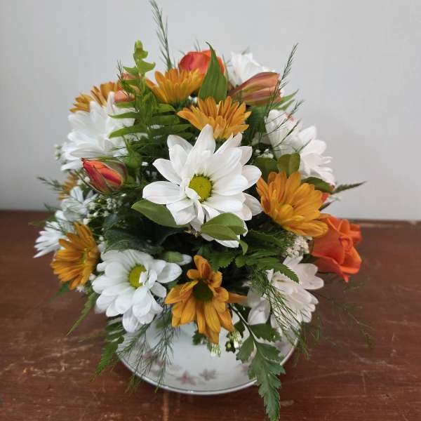 Mixed bouquet of white and orange daisies in a white vase