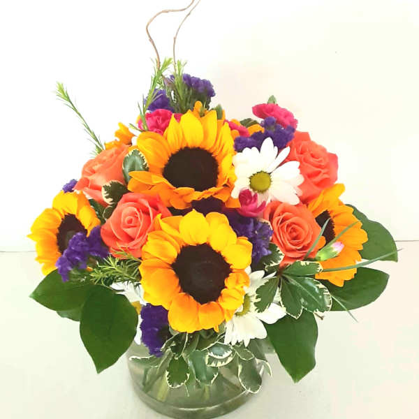 Mixed bouquet with sunflowers, roses, and daisies in a glass vase topped with a butterfly