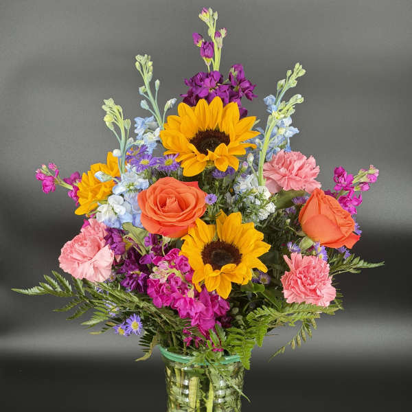 Colorful mixed bouquet in a clear glass vase with sunflowers, roses, and carnations