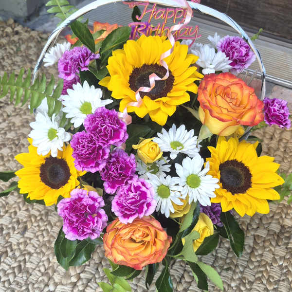 Mixed bouquet with sunflowers, roses, daisies, and carnations under a Happy Birthday topper