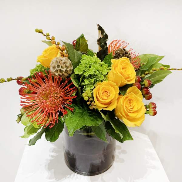 Yellow roses and red pincushion blooms in a dark vase