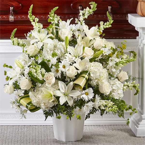 White lilies and roses arranged in a white vase with green accents.