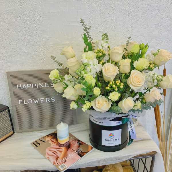 Cream roses and white blooms arranged in a black hat box with a ribbon.