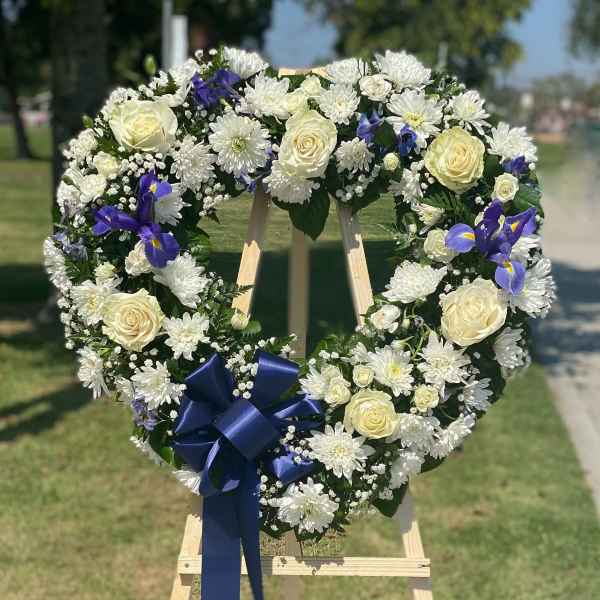 Heart-shaped floral wreath with white roses, daisies, and blue irises on an easel