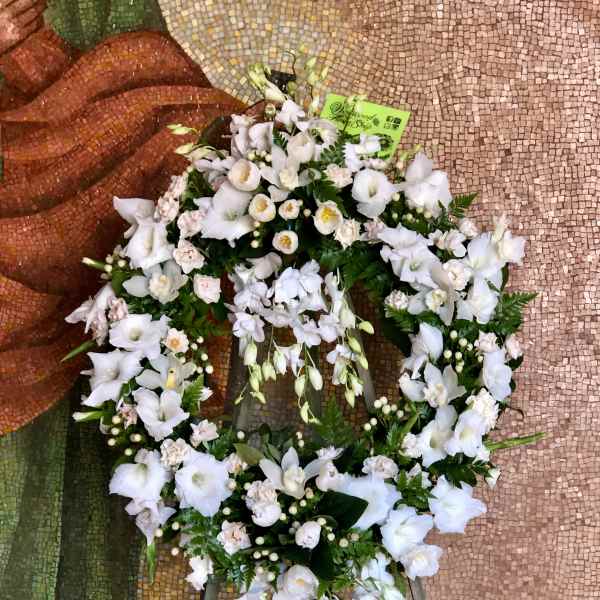 White floral wreath on a stand with trailing blooms