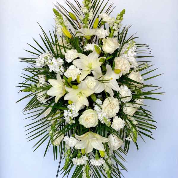White floral standing spray with lilies and roses on a palm backdrop