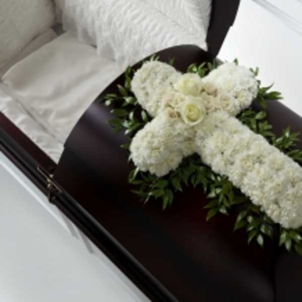White floral cross arrangement on a dark casket