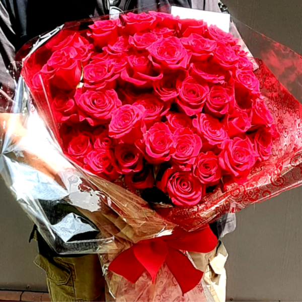 Large bouquet of bright red roses wrapped in shiny paper with a red ribbon