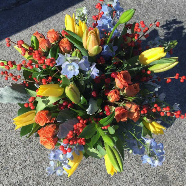 Bouquet of yellow tulips, orange roses, and blue flowers with red berry stems
