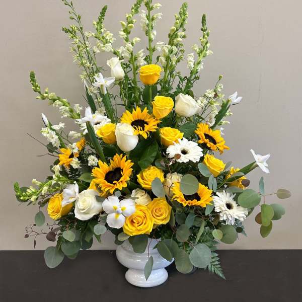 Tall yellow and white arrangement with sunflowers, roses, daisies and snapdragons in a white pedestal vase