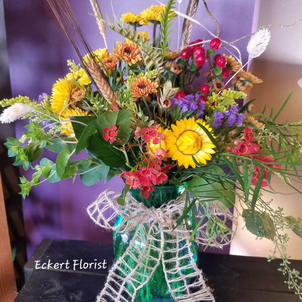 Mixed bouquet in a teal glass vase with yellow and orange flowers