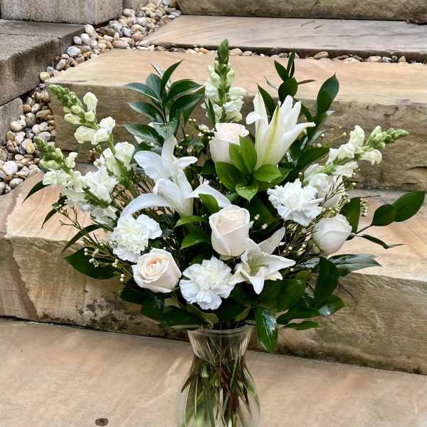 White lilies and roses arranged in a clear glass vase