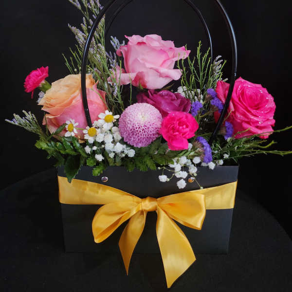 Mixed pink and purple flower arrangement in a black gift bag with a yellow ribbon