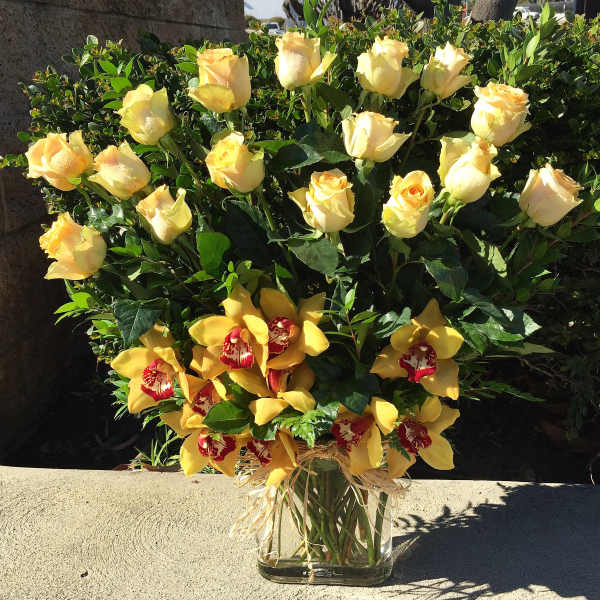 Yellow roses and orchids arranged in a clear glass vase