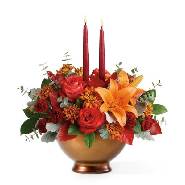 Red and orange floral arrangement in a gold bowl with two red candles