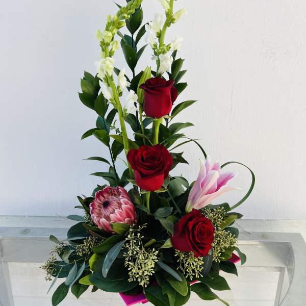 Tall floral arrangement with red roses, pink lily, and white snapdragons