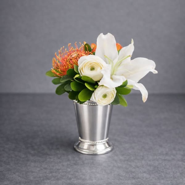 White lilies and ranunculus in a silver vase with orange blooms