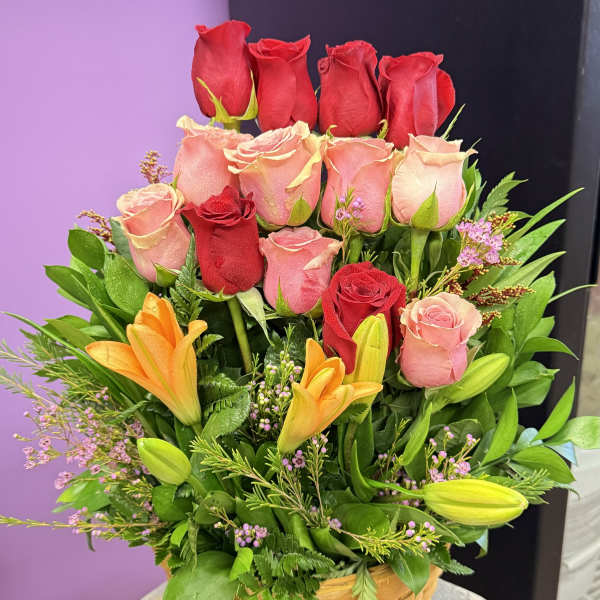 Basket arrangement of red and pink roses with orange lilies