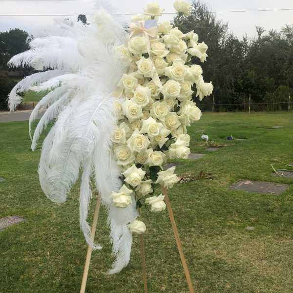 Tall white rose standing spray with large white feathers on an easel